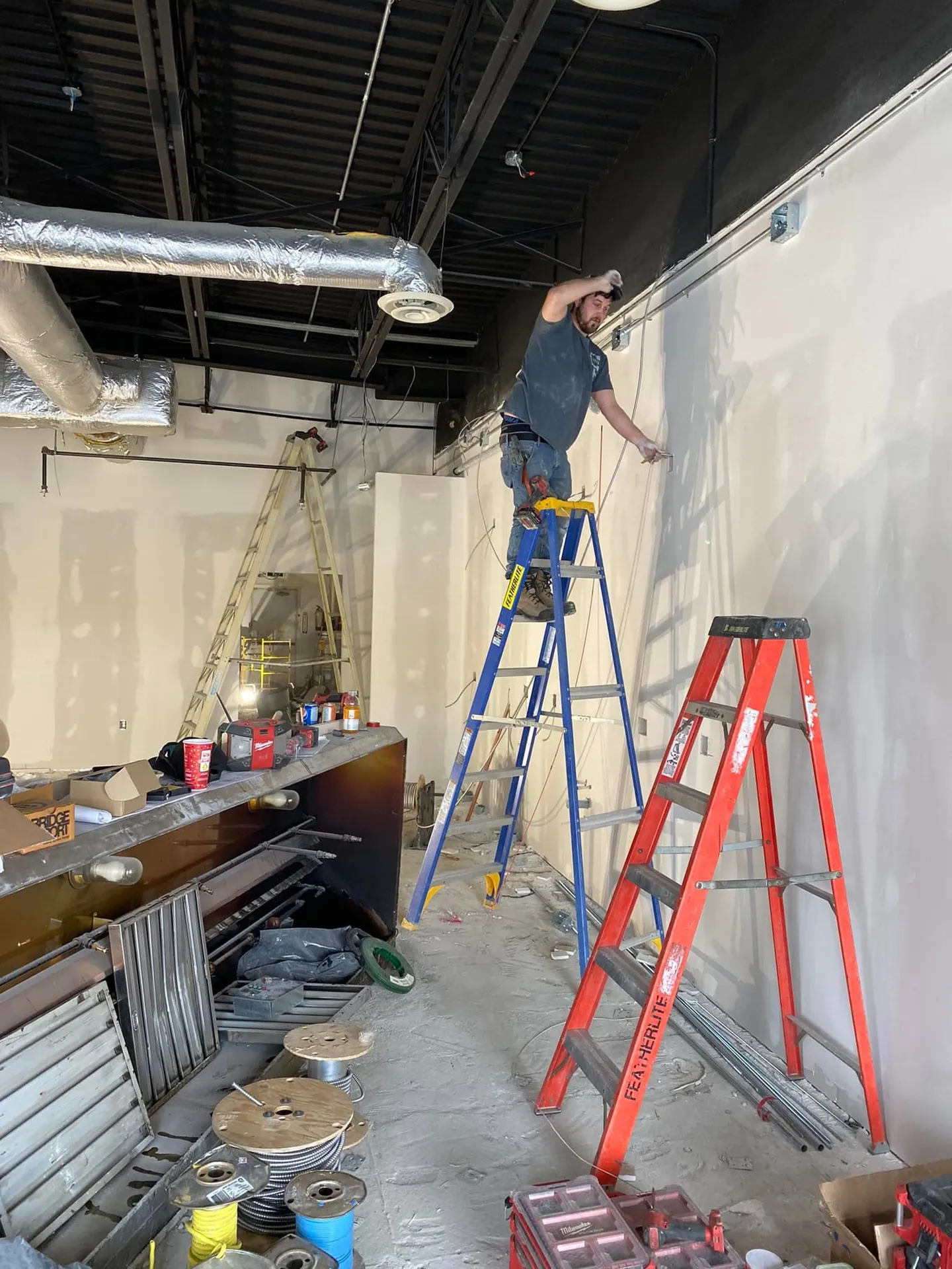 Electrician installing lighting in a commercial interior with an open ceiling.