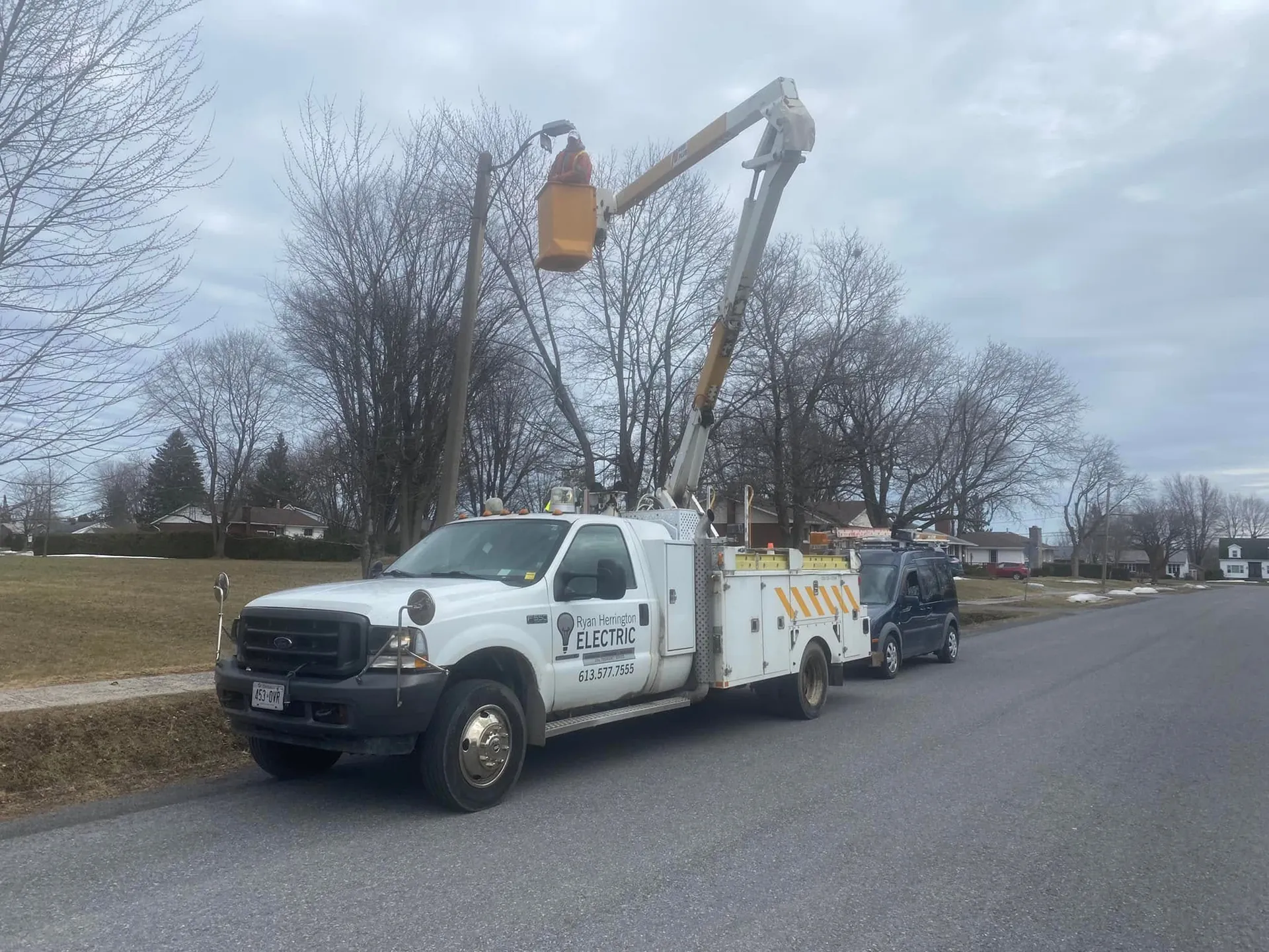 Bucket truck raised for overhead electrical work beside a residential road.